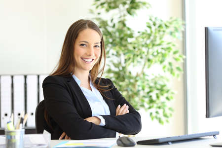 Happy businesswoman wearing suit posing sitting looking at camera at officeの写真素材