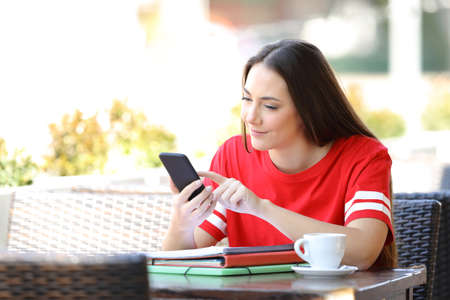 Serious student checking smart phone content sitting in a coffee shop terraceの写真素材