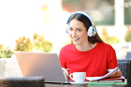 Happy student e-learning looking at camera sitting in a coffee shop terraceの写真素材