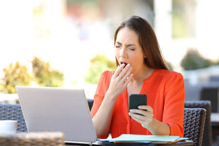 Tired entrepreneur yawning while works sitting in a coffee shop terraceの写真素材