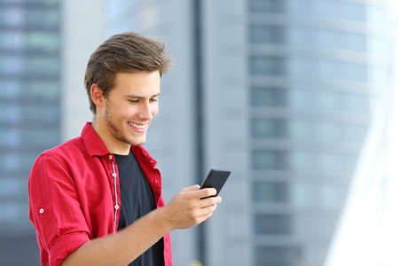 Happy entrepreneur using smart phone standing in the street with office buildings in the backgroundの写真素材