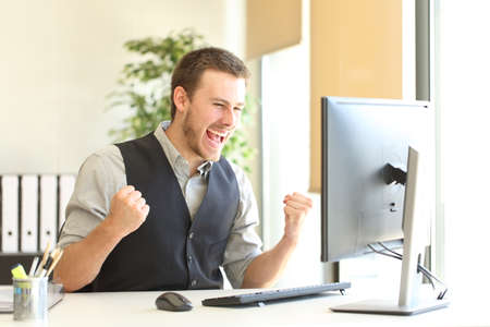 Excited businessman checking good news on computer celebrating success at officeの写真素材