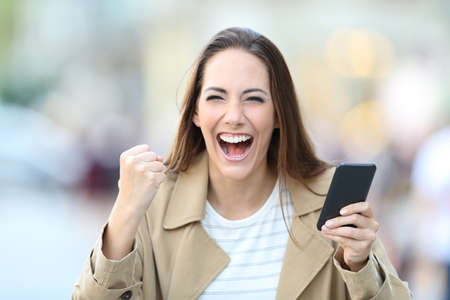 Front view portrait of excited woman holding smart phone looking at camera in the streetの写真素材
