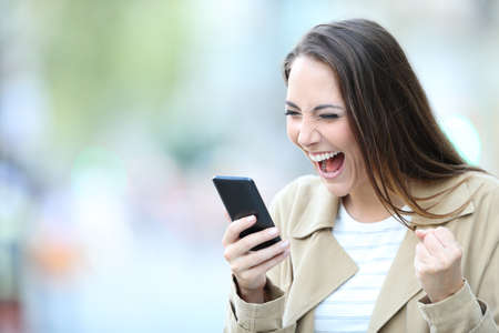 Excited woman finds good on line offers on smart phone standing in the streetの写真素材