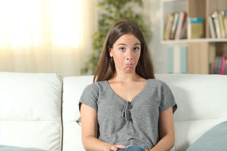 Front view portrait of a perplexed woman looking at camera sitting on a couch at homeの写真素材