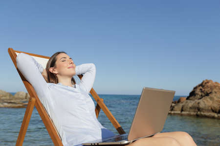 Relaxed entrepreneur resting sitting on a deck chair on the beach with a laptop on legsの写真素材