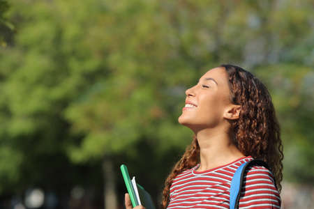 Happy mixed race student breathing deeply fresh air standing in a park or campusの写真素材