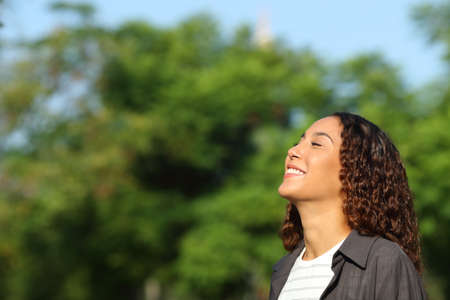 Happy mixed race woman breathing deeply fresh air in a park or forest a sunny dayの写真素材