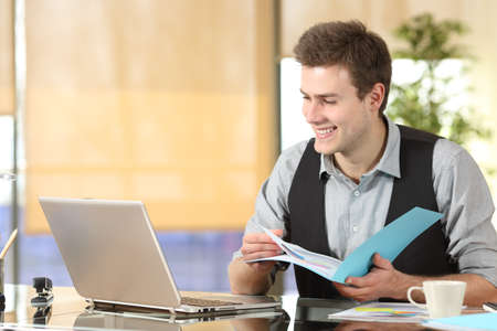 Happy worker comparing laptop online content and paper documents at officeの写真素材
