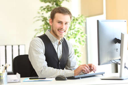 Happy executive posing looking at camera with the hands on computer keyboard at officeの写真素材