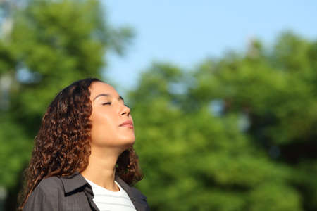 Relaxed mixed race woman breathing deeply fresh air in a park or forest a sunny dayの写真素材