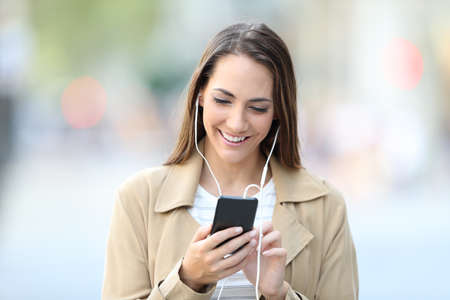 Front view portrait of a happy girl listening to music walking towards camera in the streetの写真素材