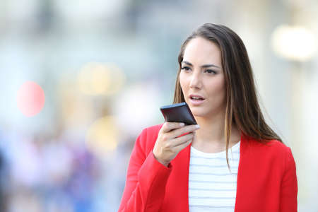 Serious woman in red using voice recognition to dictate messages on smart phone in the streetの写真素材