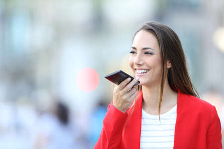 Happy woman in red using voice recognition on smart phone to dictate message in the streetの写真素材