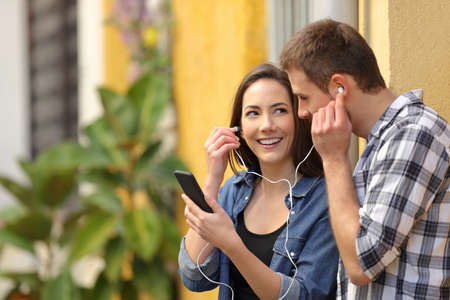 Happy couple sharing earphones to listen to the music online from smart phone in a colorful streetの写真素材