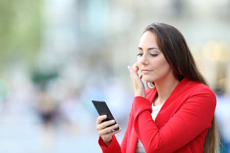 Fashion woman in red using smart phone as a mirror to comb her hair in the streetの写真素材