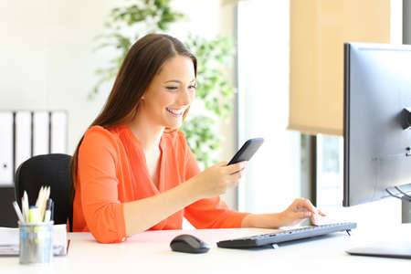 Happy entrepreneur in orange checking smart phone message at officeの写真素材