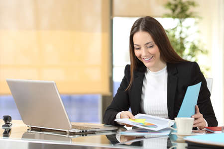 Happy executive checking paper documents sitting at officeの写真素材