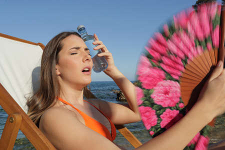 Stressed woman suffering heat stroke fanning sitting on a deck chair on the beach in a extremely warm day on vacationの写真素材