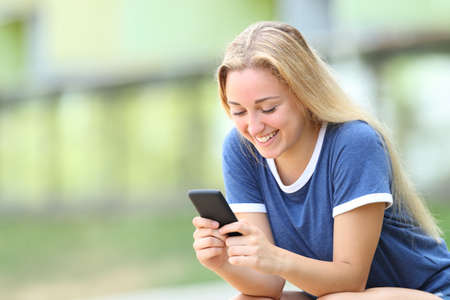 Happy teenage girl texing messages on smart phone sitting in an university campusの写真素材