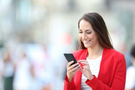 Happy elegant woman in red using smart phone standing in the streetの写真素材