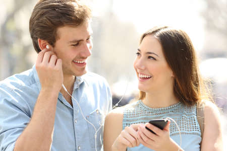 Front view of a happy couple walking listening to music sharing earphones in the streetの写真素材