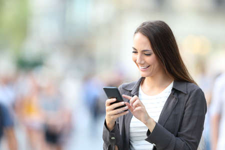 Happy casual woman checking smart phone on line content standing in the streetの写真素材