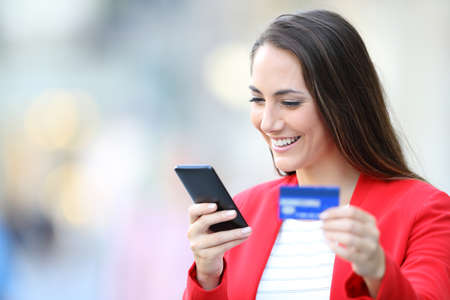 Happy woman in red buying on line with smart phone and credit card in the streetの写真素材