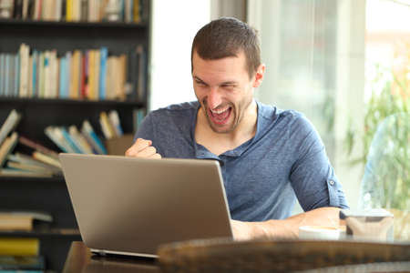 Excited adult man finding laptop online content celebrating success sitting in a bar or homeの写真素材