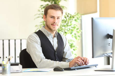 Confident executive posing looking at camera with the hands on computer keyboard at officeの写真素材