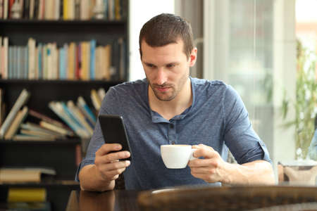 Serious man checking smart phone online content sitting in a coffee shopの写真素材