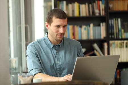 Serious adult man writing on laptop entering data sitting in a coffee shop or homeの写真素材