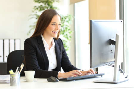 Happy executive is using a computer entering data at officeの写真素材