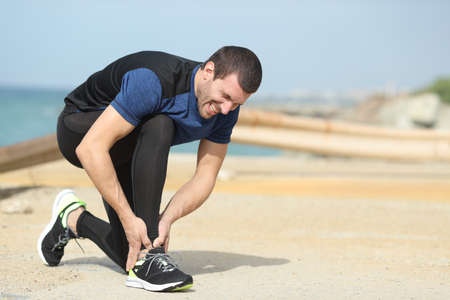 Painful runner complaining suffering ankle ache on the beach after sportの写真素材