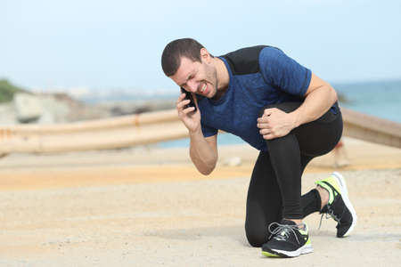 Painful runner suffering knee ache asking for help calling on phoneの写真素材