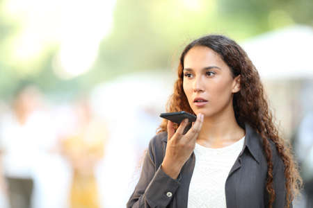 Serious mixed race woman using voice recognition on smart phone walking in the streetの写真素材