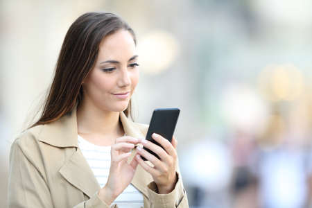 Serious lady browsing smart phone online content walking in the streetの写真素材