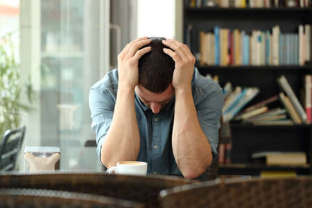 Front view portrait of a sad man complaining alone in a coffee shopの写真素材