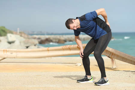 Painful runner complaining suffering back ache after sport on the beachの写真素材