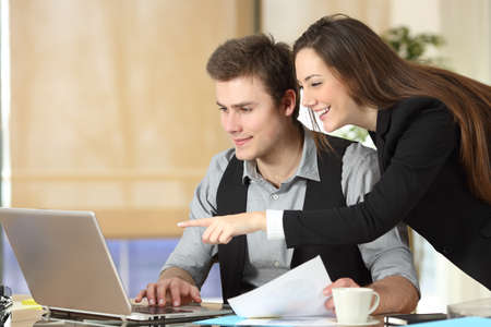 Happy businesswoman showing laptop content to her colleague at officeの写真素材