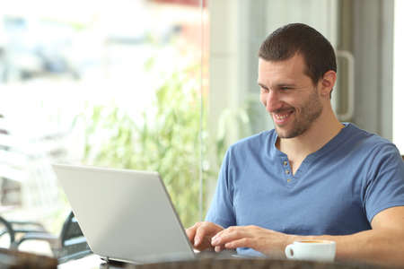 Happy adult man using a laptop writing content sitting in a coffee shopの写真素材