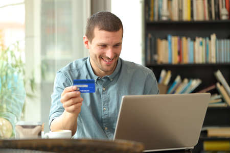Happy adult buyer buying online with credit card and laptop sitting in a coffee shop or homeの写真素材
