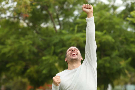 Excited happy casual man raising arm celebrating success alone in a parkの写真素材