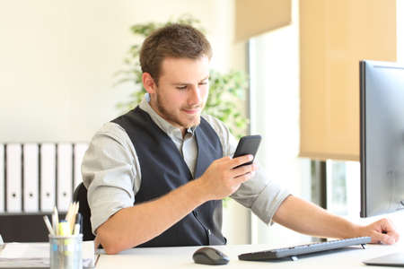 Serious executive checking smart phone message sitting at officeの写真素材