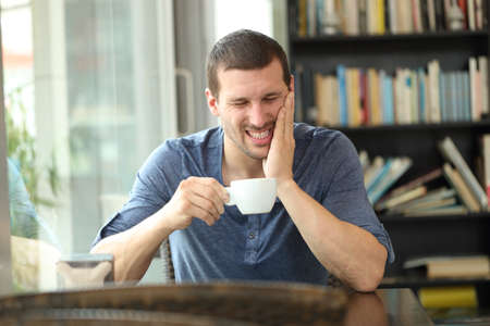 Fronf view portrait of a man complaining suffering tooth ache after drinking hot beverage sitting in a coffee shopの写真素材