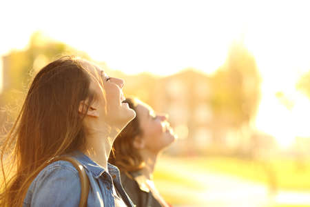 Profile of two happy friends breathing deep fresh air at sunset in a parkの写真素材