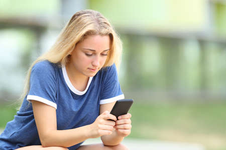 Serious  teenage girl texing message on smart phone sitting in an university campusの写真素材