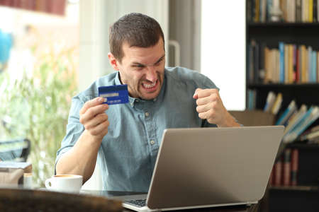 Angry man having problems to pay online with credit card sitting in a coffee shopの写真素材