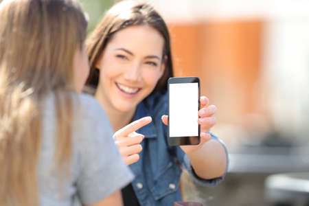 Happy girl shows blak smart phone screen to her friend in the streetの写真素材