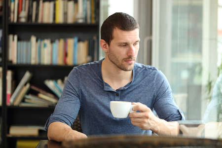 Pensive sad man looks away through a window in a coffee shop or homeの写真素材
